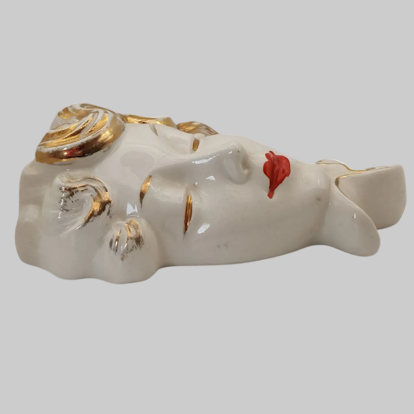 Decorative chalkware face with gold accents and red lips on a white background