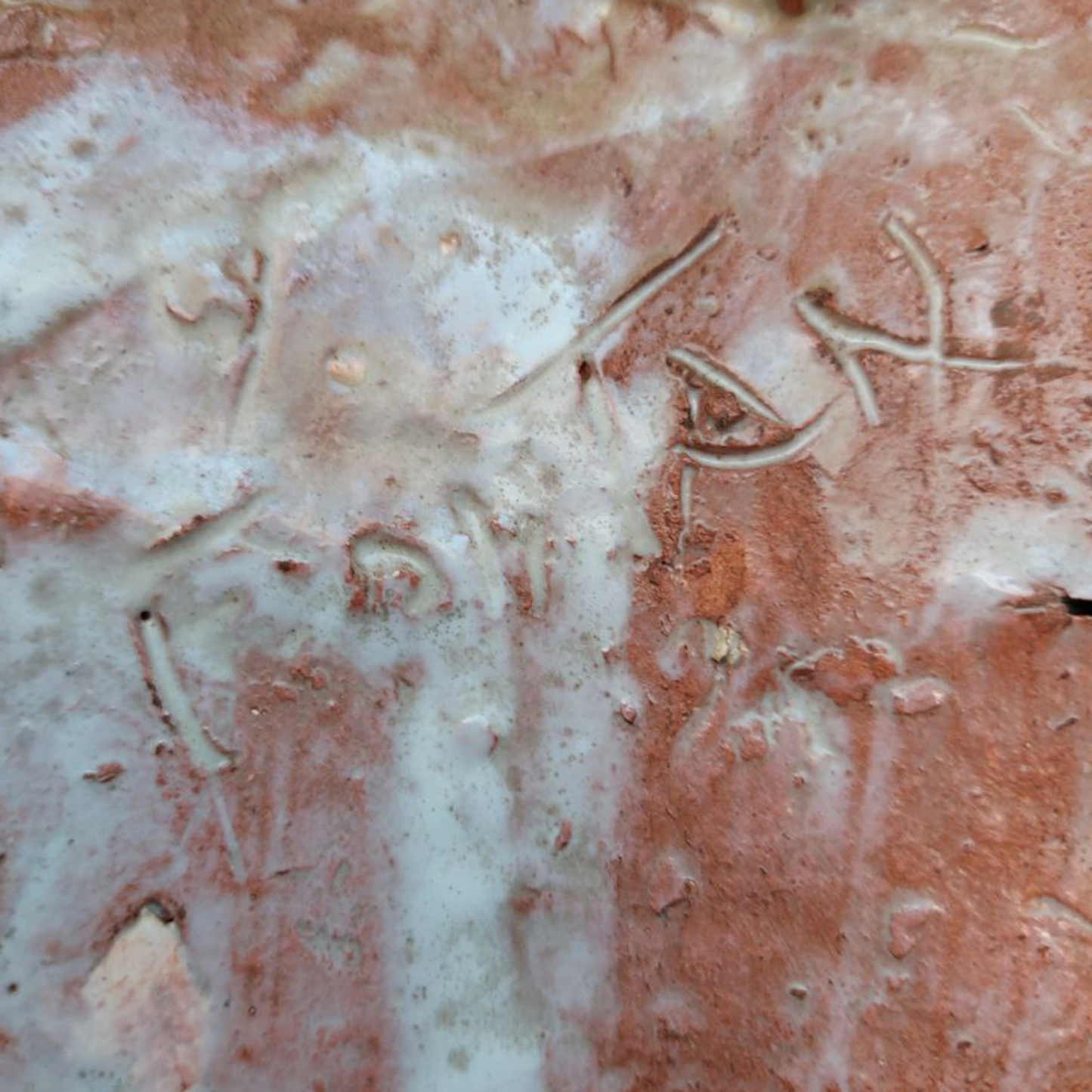 Close-up of a textured clay surface with engraved signature.