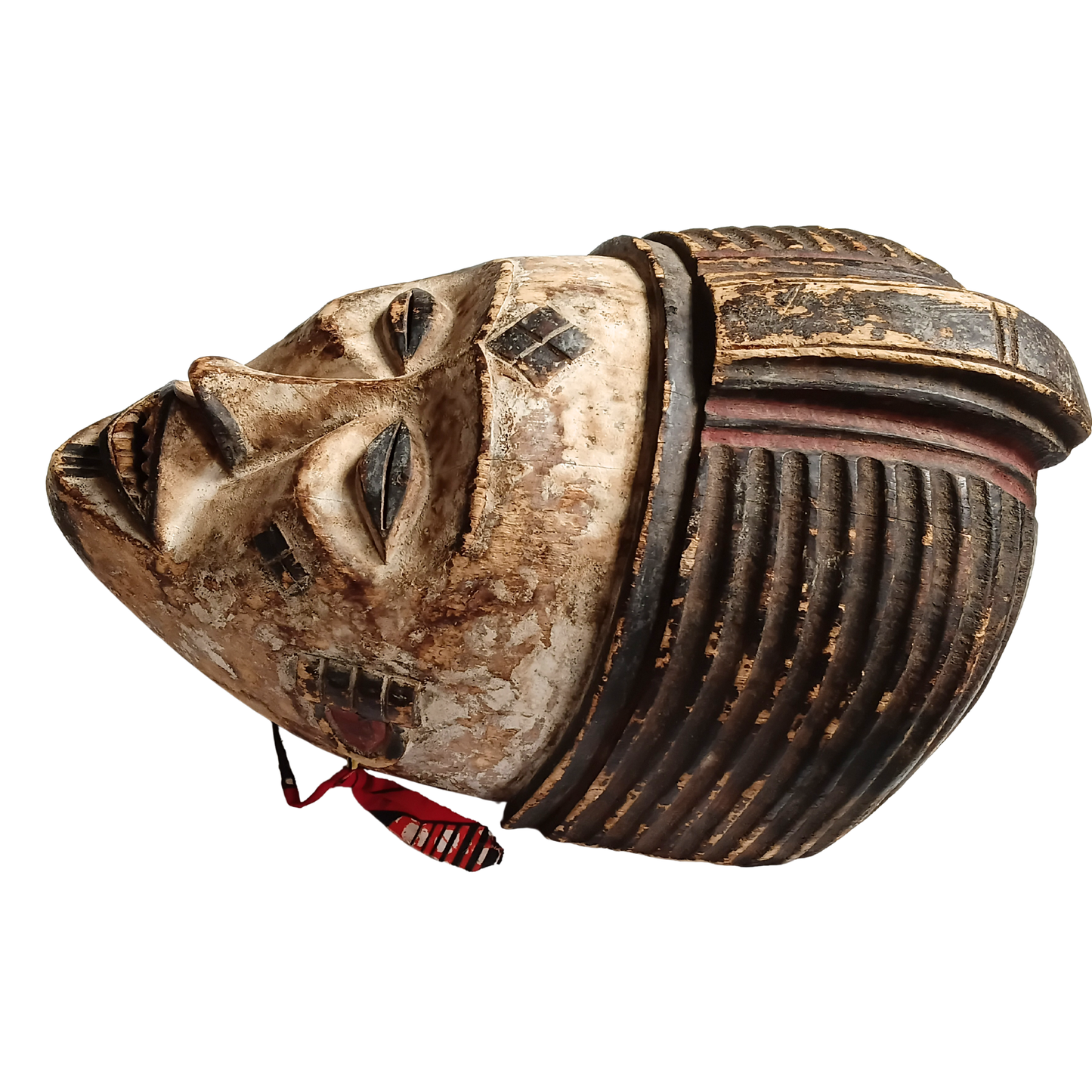 An African-style carved wooden mask with a weathered beige face, dark brown ribbed headpiece, and a small red hanging tassel, shown on a plain white background.