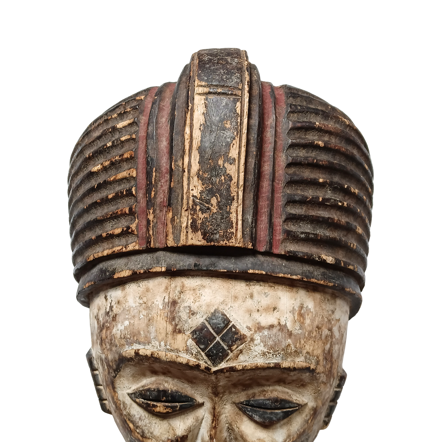 An antique African wooden mask with a weathered face, detailed with a striped, ribbed hat-like headdress in dark brown and reddish-brown tones, set against a plain white background.