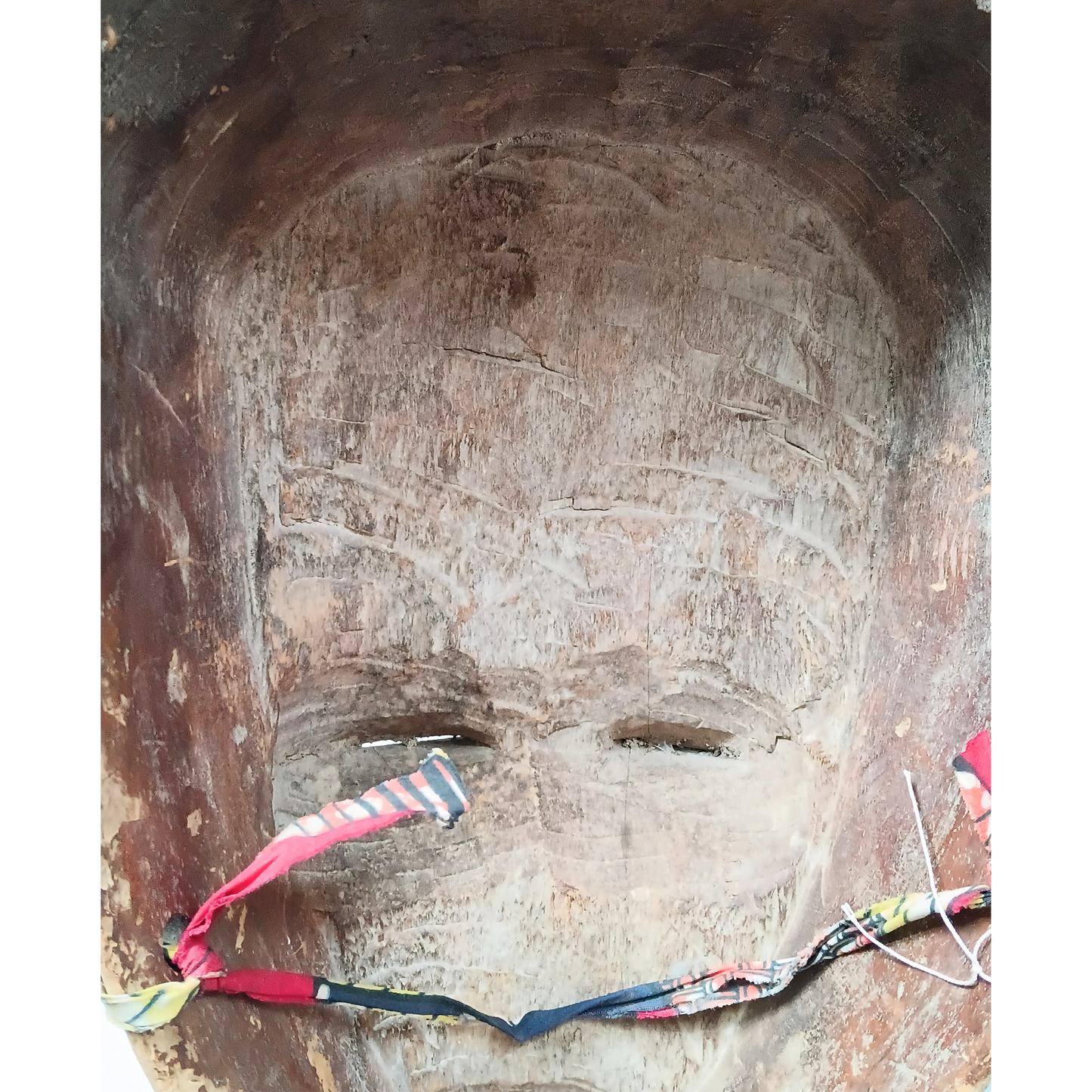 A close-up of a large carved African style mask with a ribbon tied across the mouth and nose area.