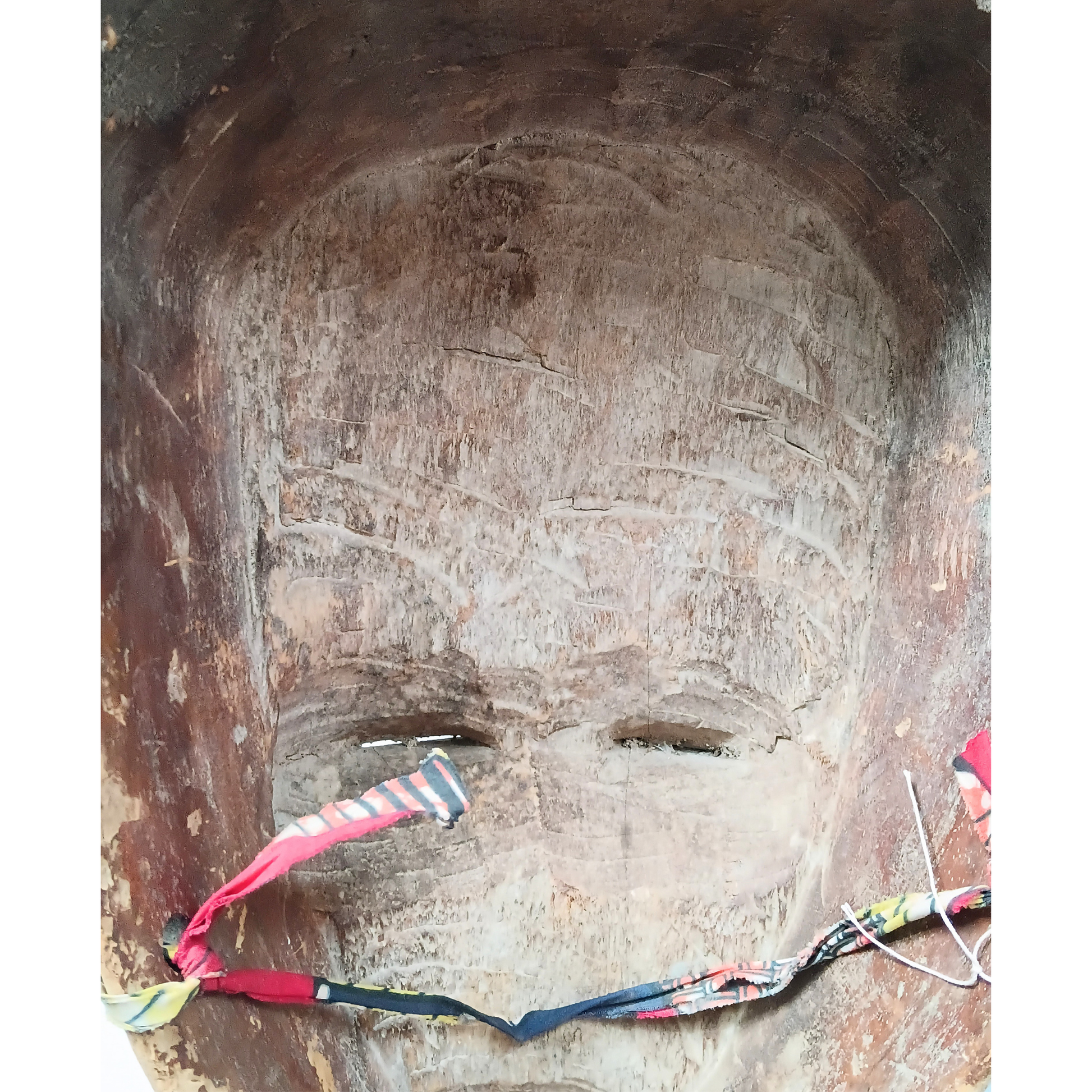 A close-up of a large carved African style mask with a ribbon tied across the mouth and nose area.