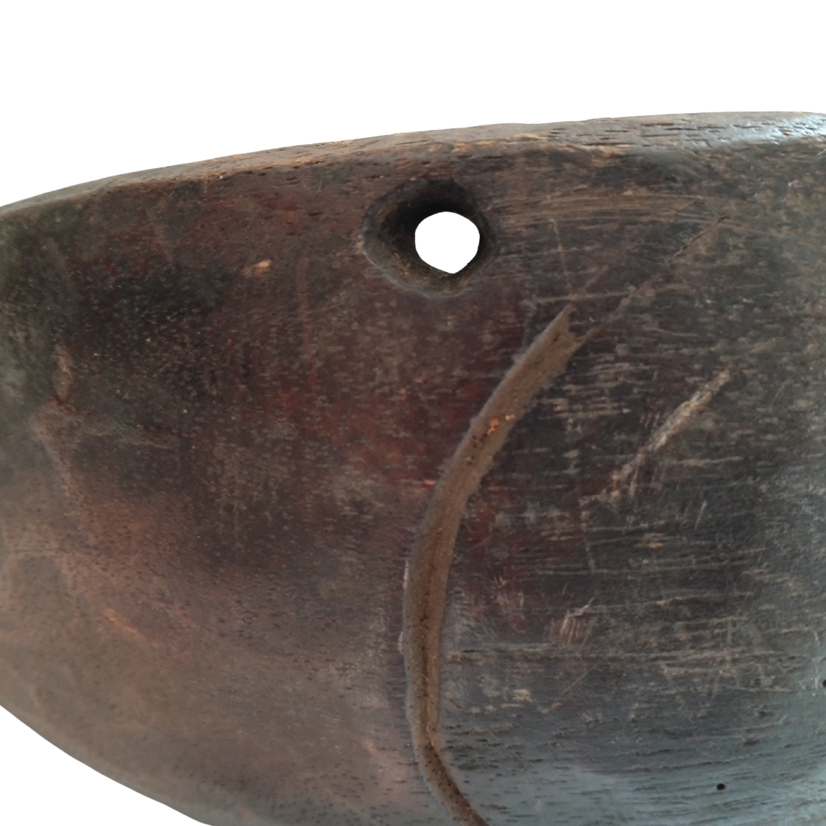Close-up of a dark brown carved wooden spoon with a circular hole near the top edge and a curved carved line on the side, shown against a white background.