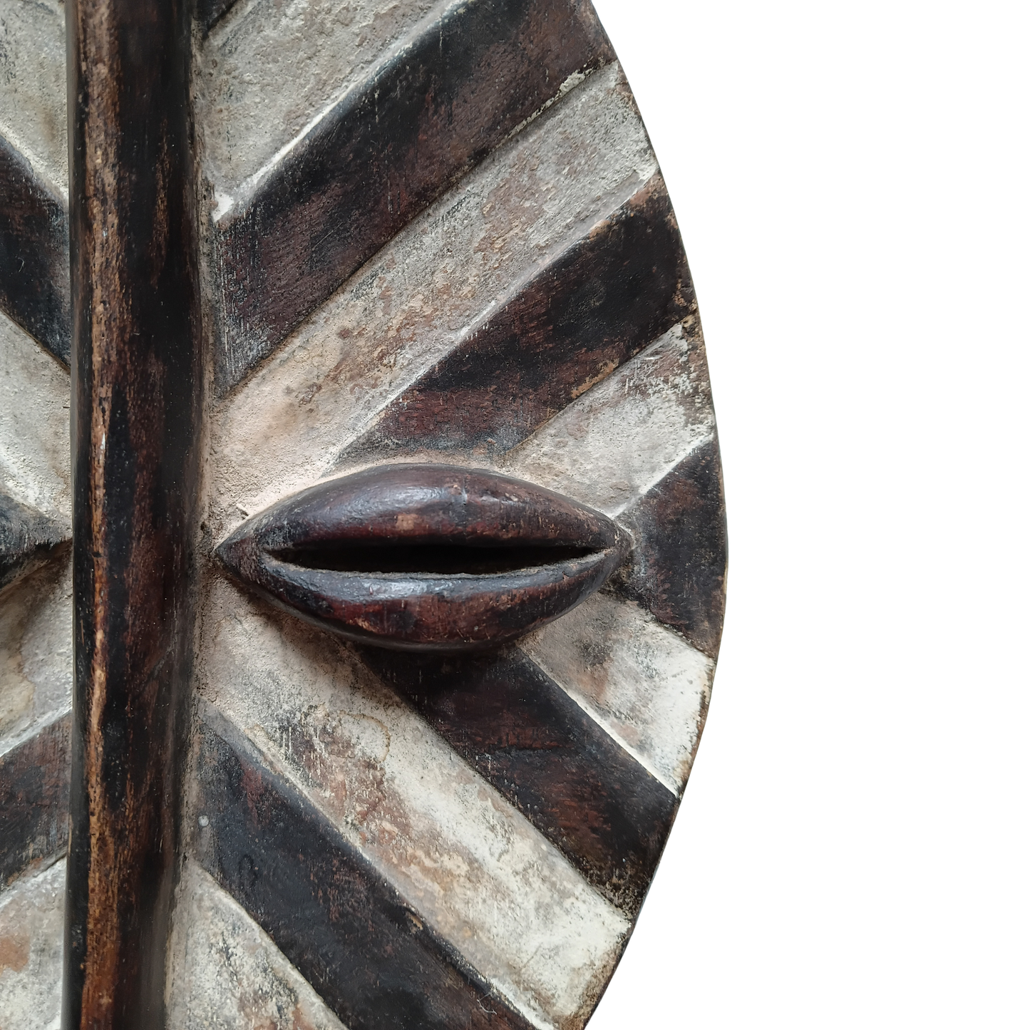 Close-up of a carved wooden mask with a stylised eye radiating carved stripes, shown against a plain white background.