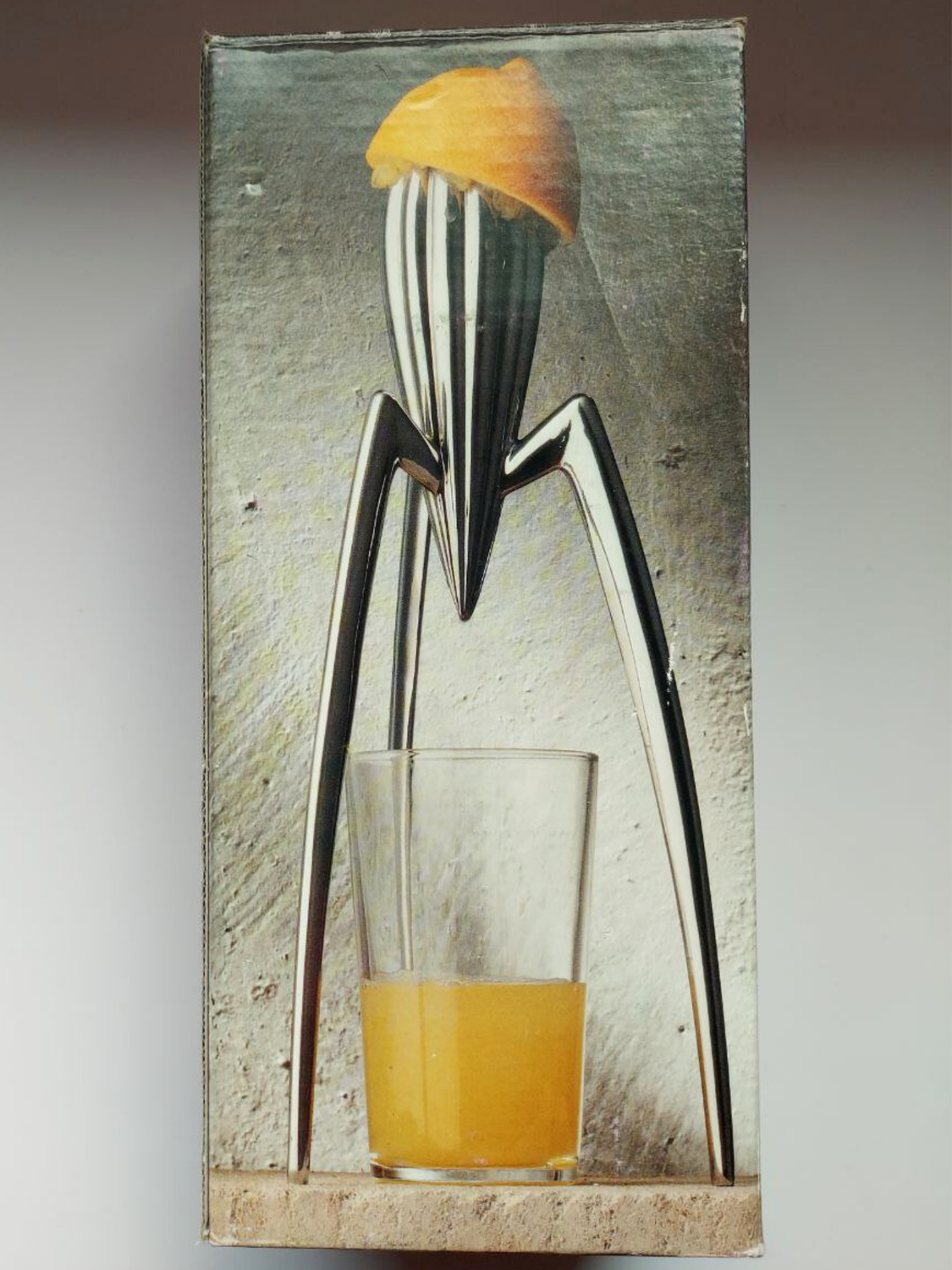 Metallic citrus squeezer with a glass of orange juice on a textured surface