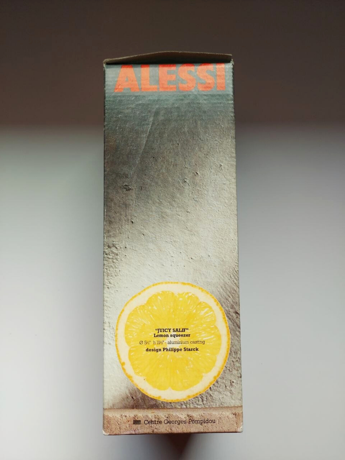 Alessi juicer packaging with a lemon illustration on a grey background