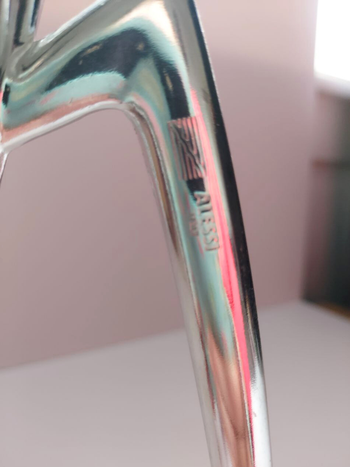 Close-up of the Alessi logo on a shiny metal object with a blurred background