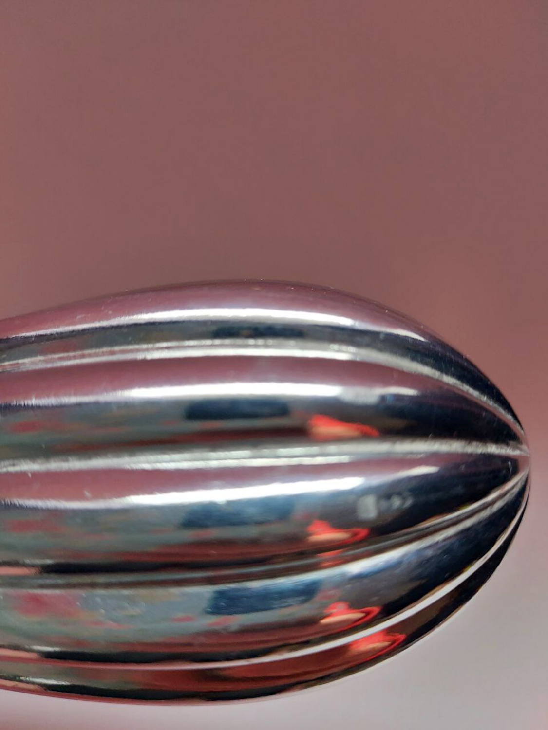Close-up of a metallic object with reflective surface on a pink background