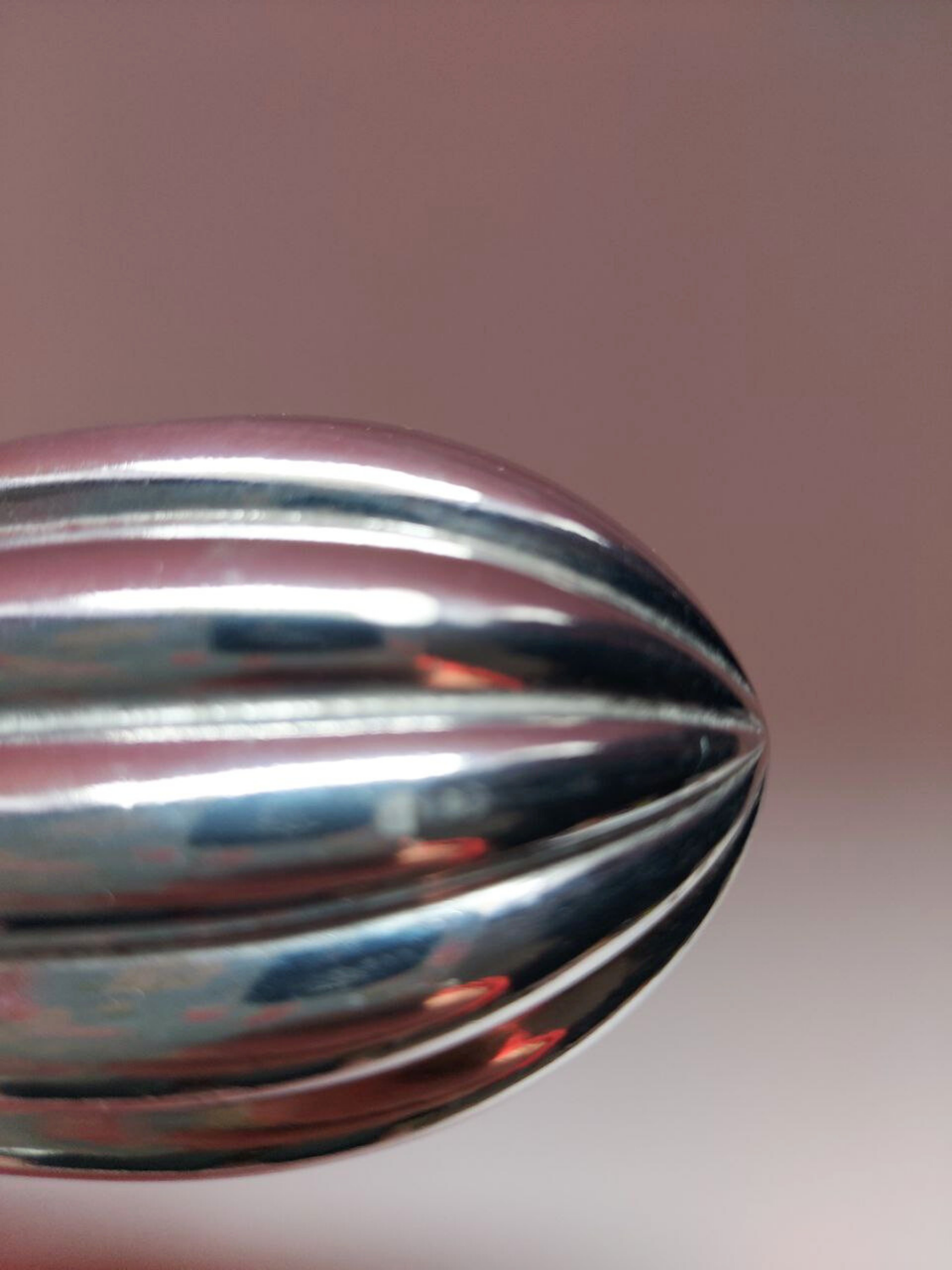 Close-up of a metallic object with reflective surface on a pink background