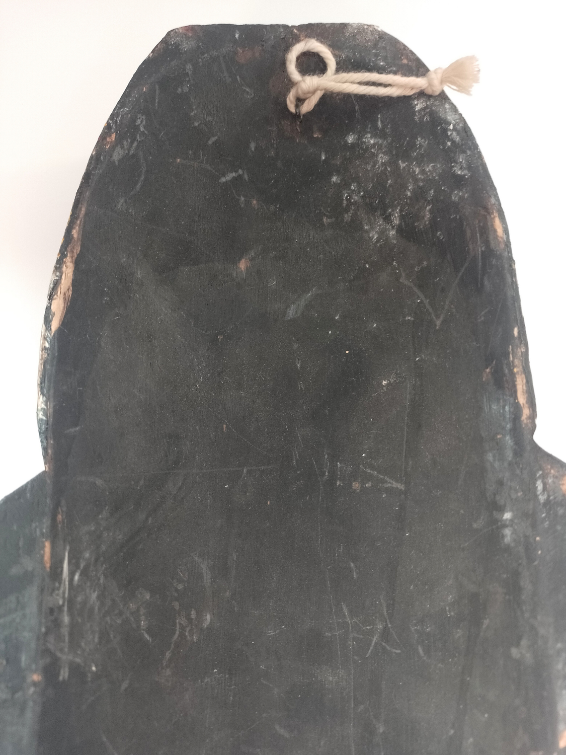 Dark wooden mask with a string tied around the top on a white background