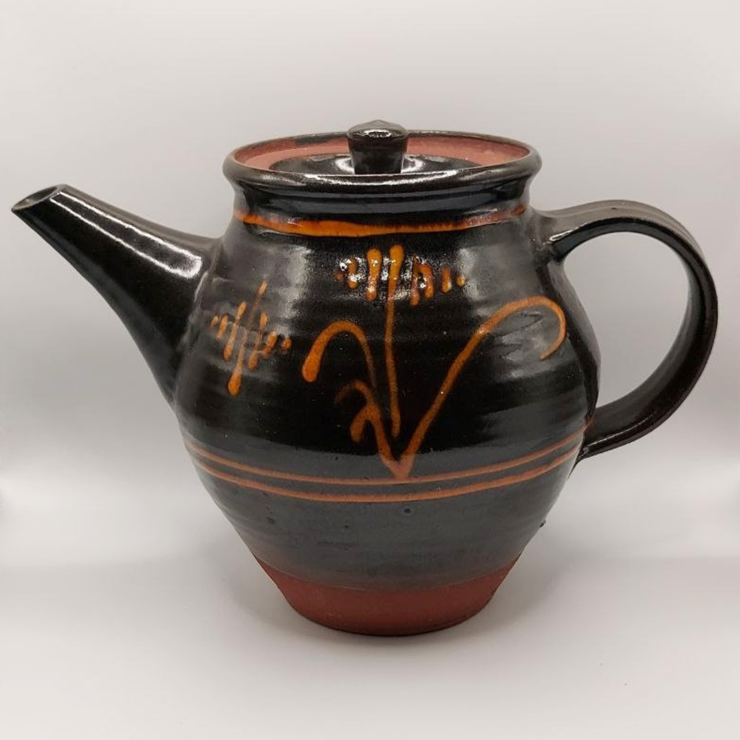 Brown ceramic teapot with orange patterns on a white background