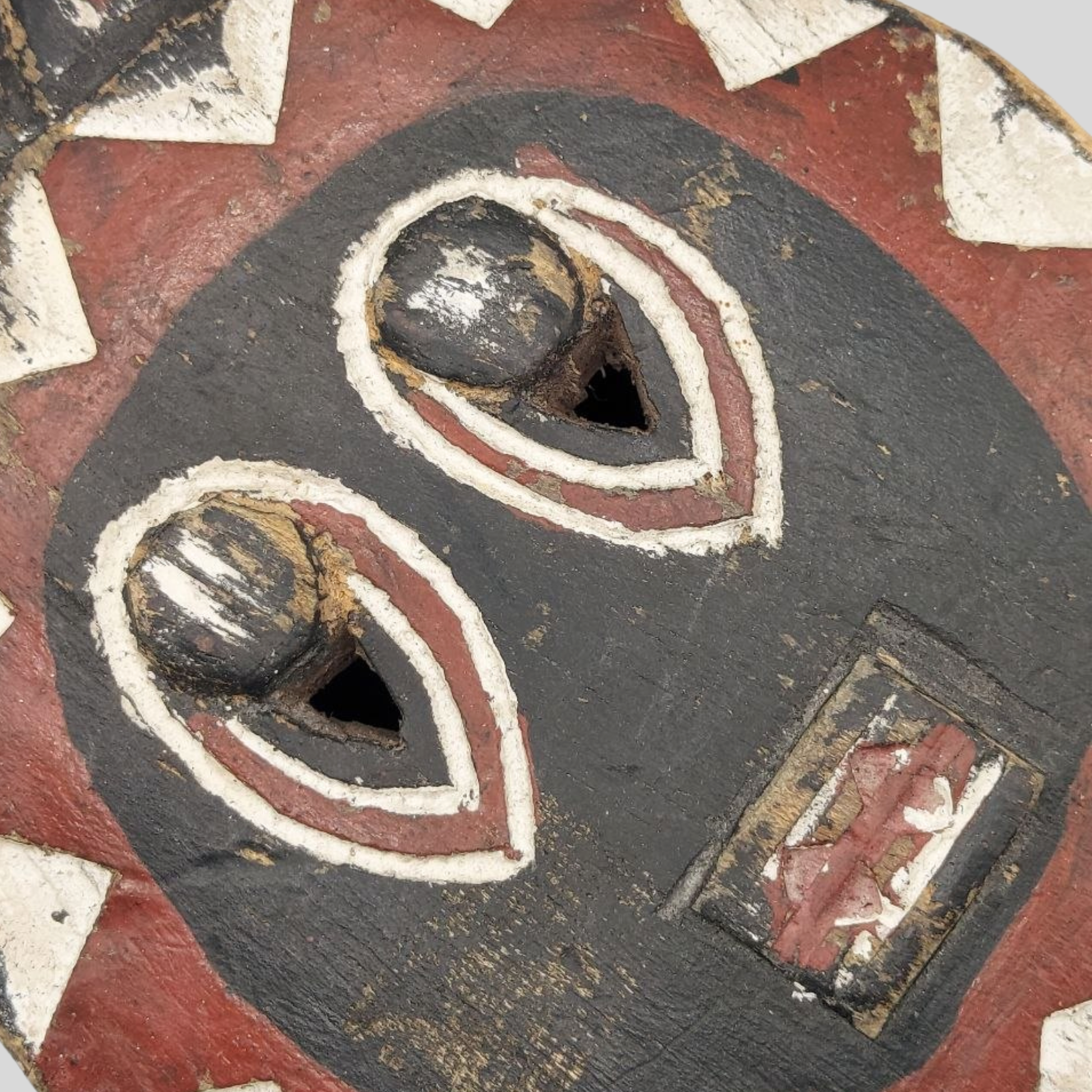 Close-up of a wooden mask with black, red, and white patterns