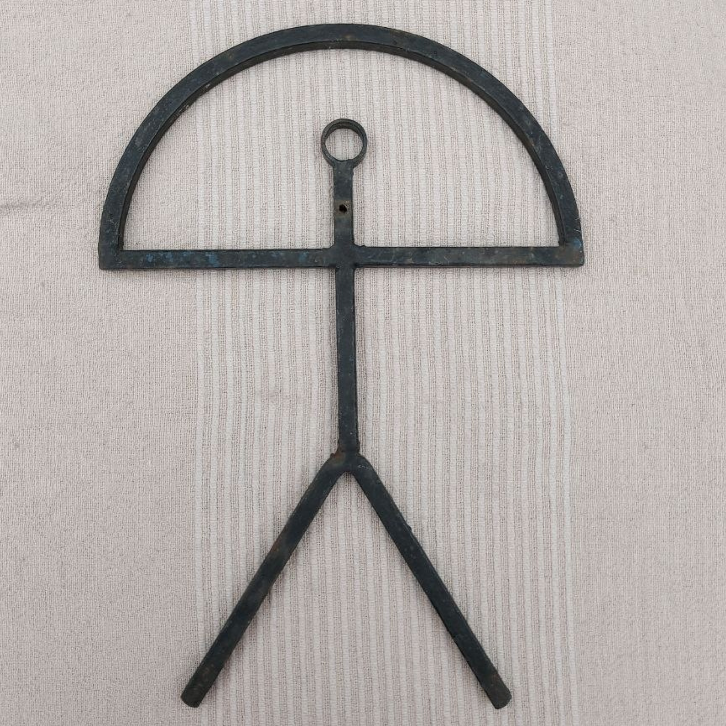 Metal object with a curved top and two legs on a textured beige background