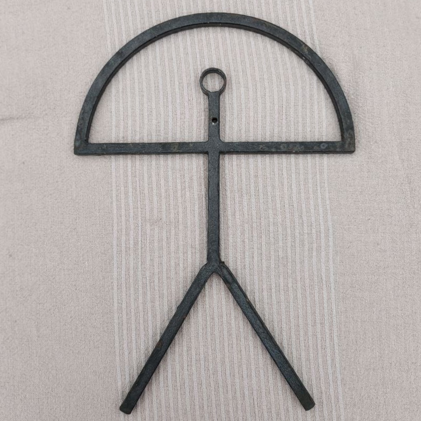 Black metal sculpture with a circular top and two legs on a beige background