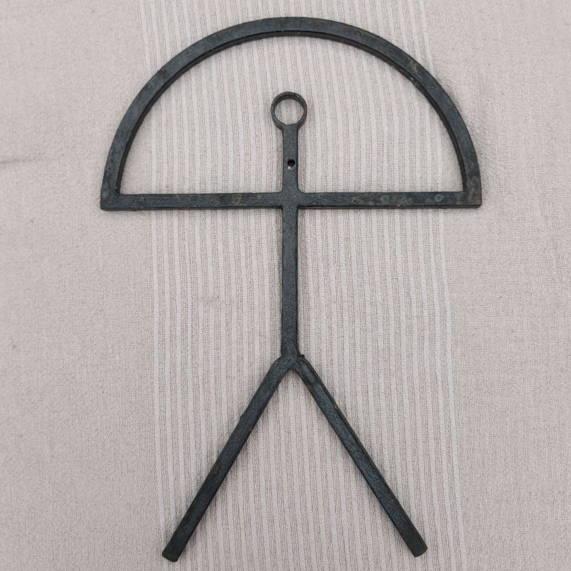 Black metal sculpture with a circular top and two legs on a beige background
