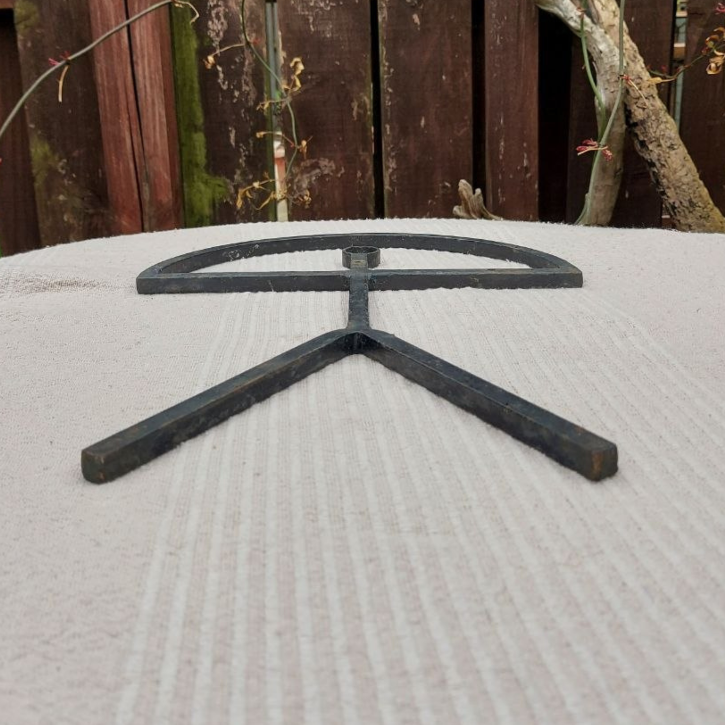 Black metal sculpture on a textured surface with a wooden fence background
