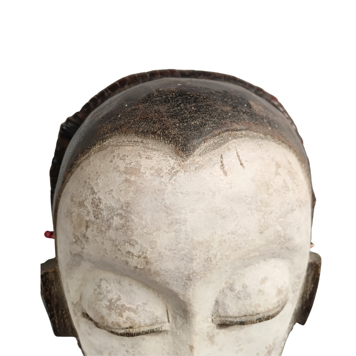 A close-up of a carved wooden mask with closed eyes, a weathered off-white face, and dark brown hair, shown against a plain white background.