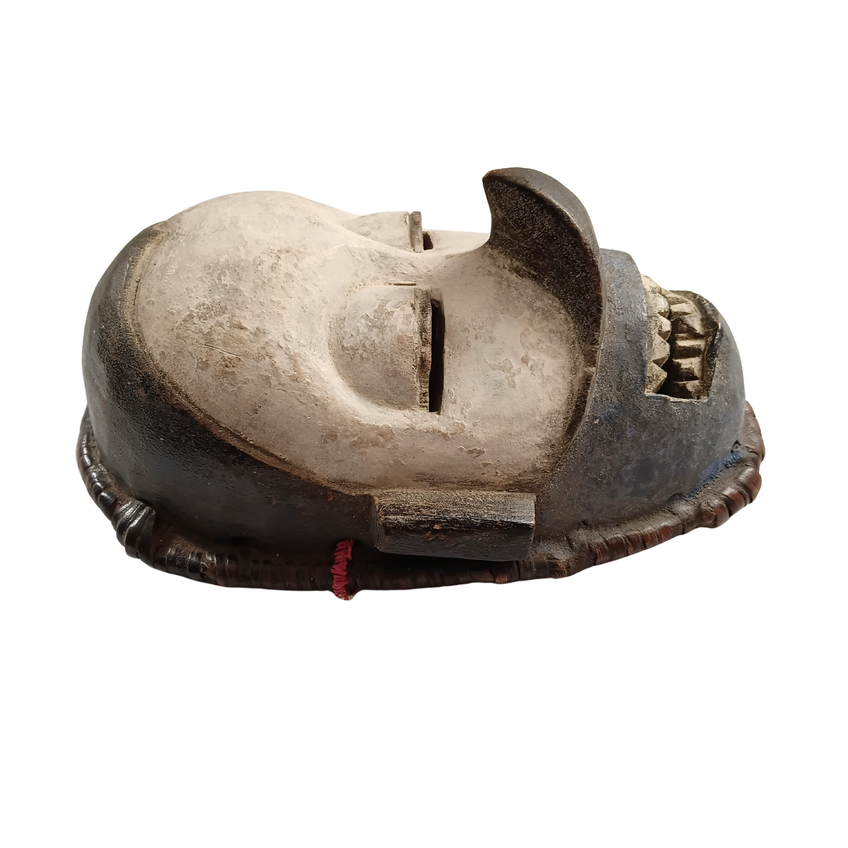 A carved wooden African-style mask with a weathered finish, featuring a large central eye opening, textured details, and a small red cord tied to the base, shown against a plain white background.