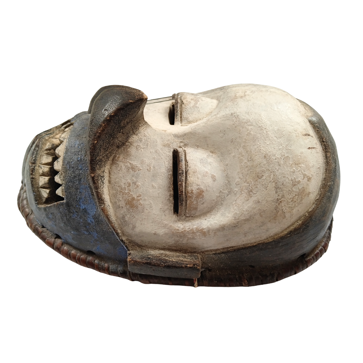 A carved wooden mask with a stylised face, featuring a weathered off-white centre and dark brown to black painted sections on the sides and mouth area, isolated on a white background.
