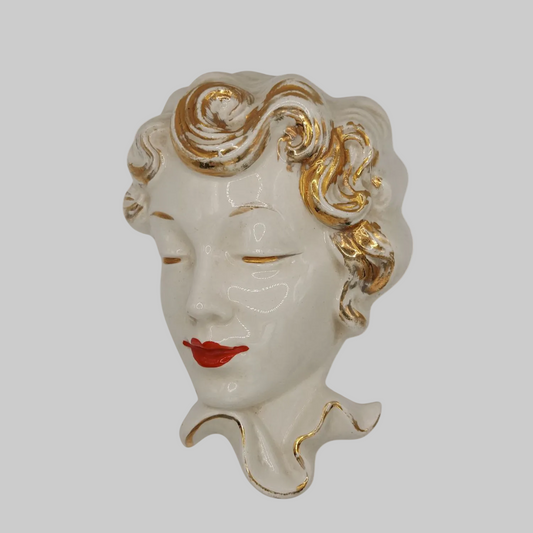 Decorative wall piece of a woman's face with gold hair and red lips on a white background