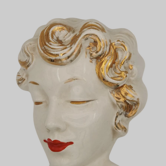 Decorative head sculpture of a woman with gold hair and red lips on a white background