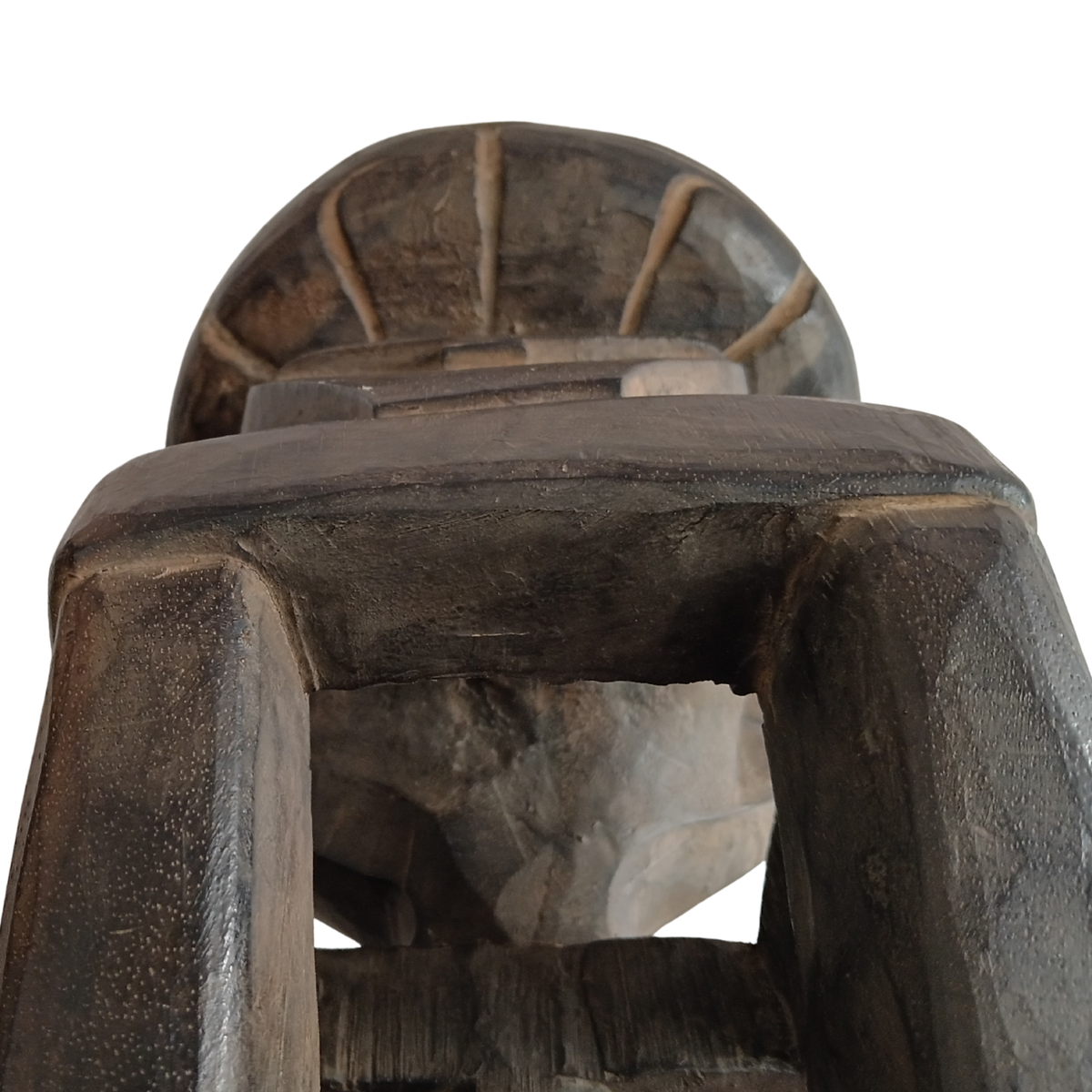 A close-up of a dark carved wooden stool with a textured finish, shown against a solid white background.