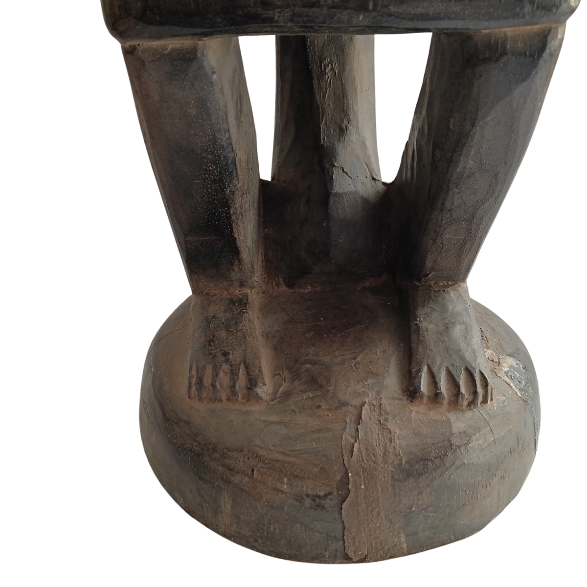 Close-up of a dark carved wooden stool or pedestal with a sculpted base featuring two legs and feet, shown against a plain white background.