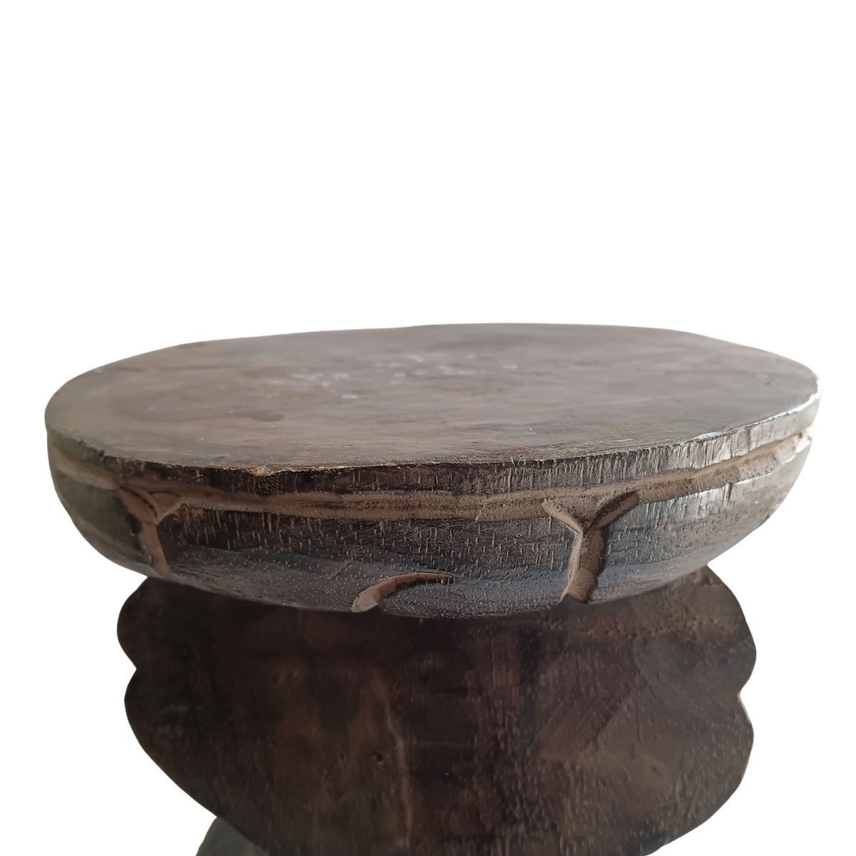 A rustic dark brown wooden stool with a thick round top and carved legs, shown against a plain white background.