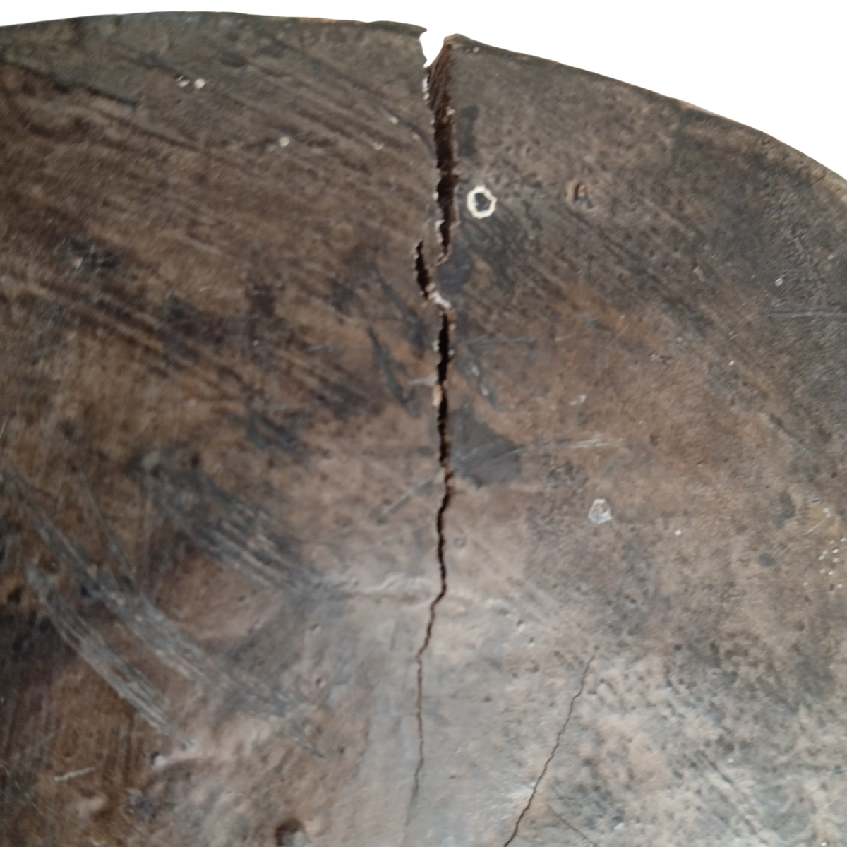 A close-up of a dark brown wooden stool top with visible grain, scratches, and a vertical crack running down the centre, against a white background.