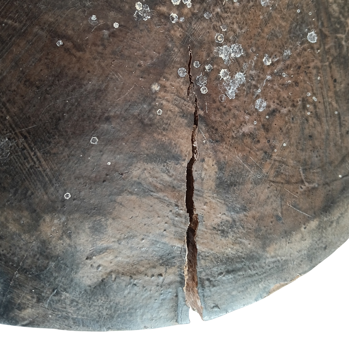 A close-up of a dark brown wooden stool top with a prominent vertical crack running down the centre and scattered small white circular marks on the surface.