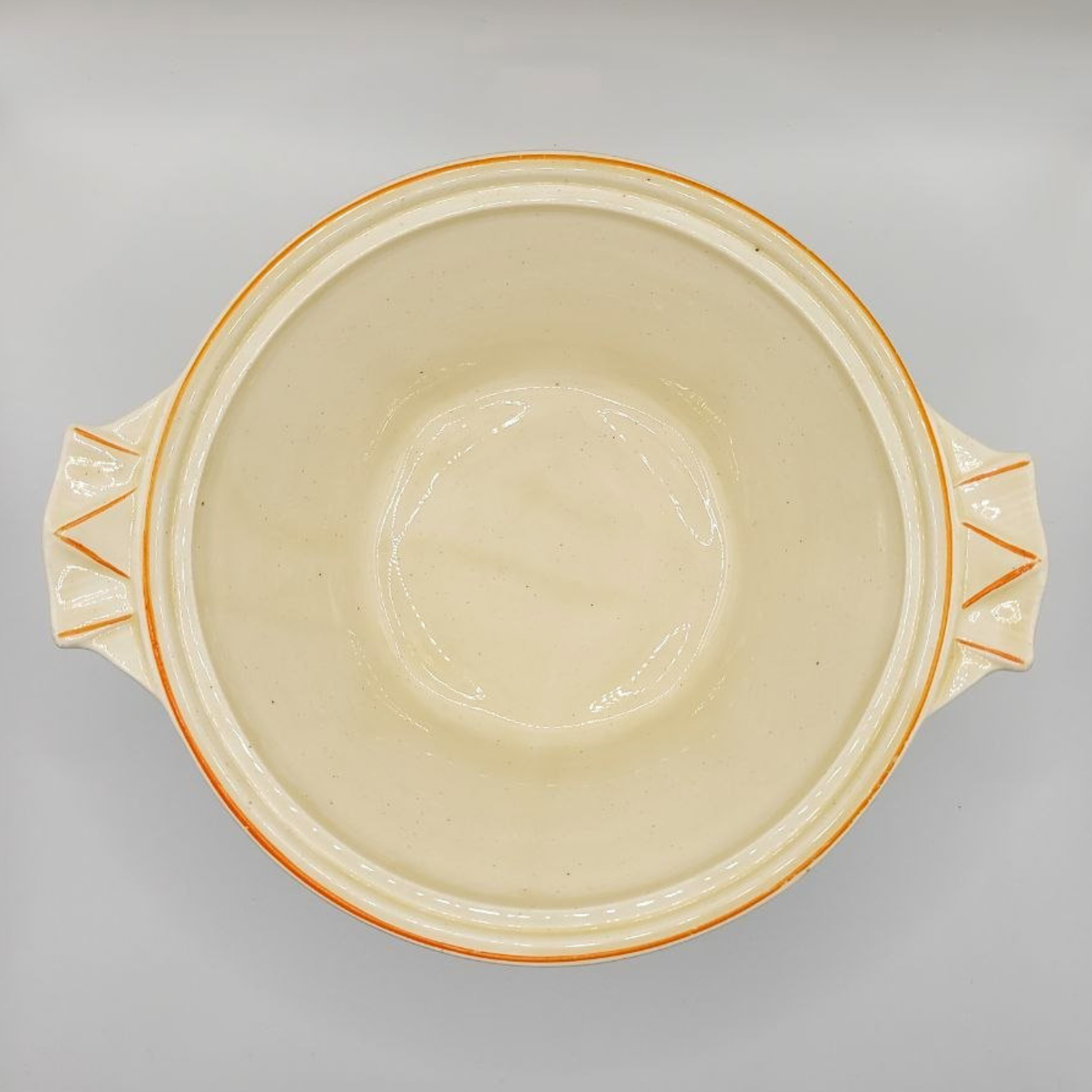 Cream-colored ceramic bowl with orange rim and handles on a grey background