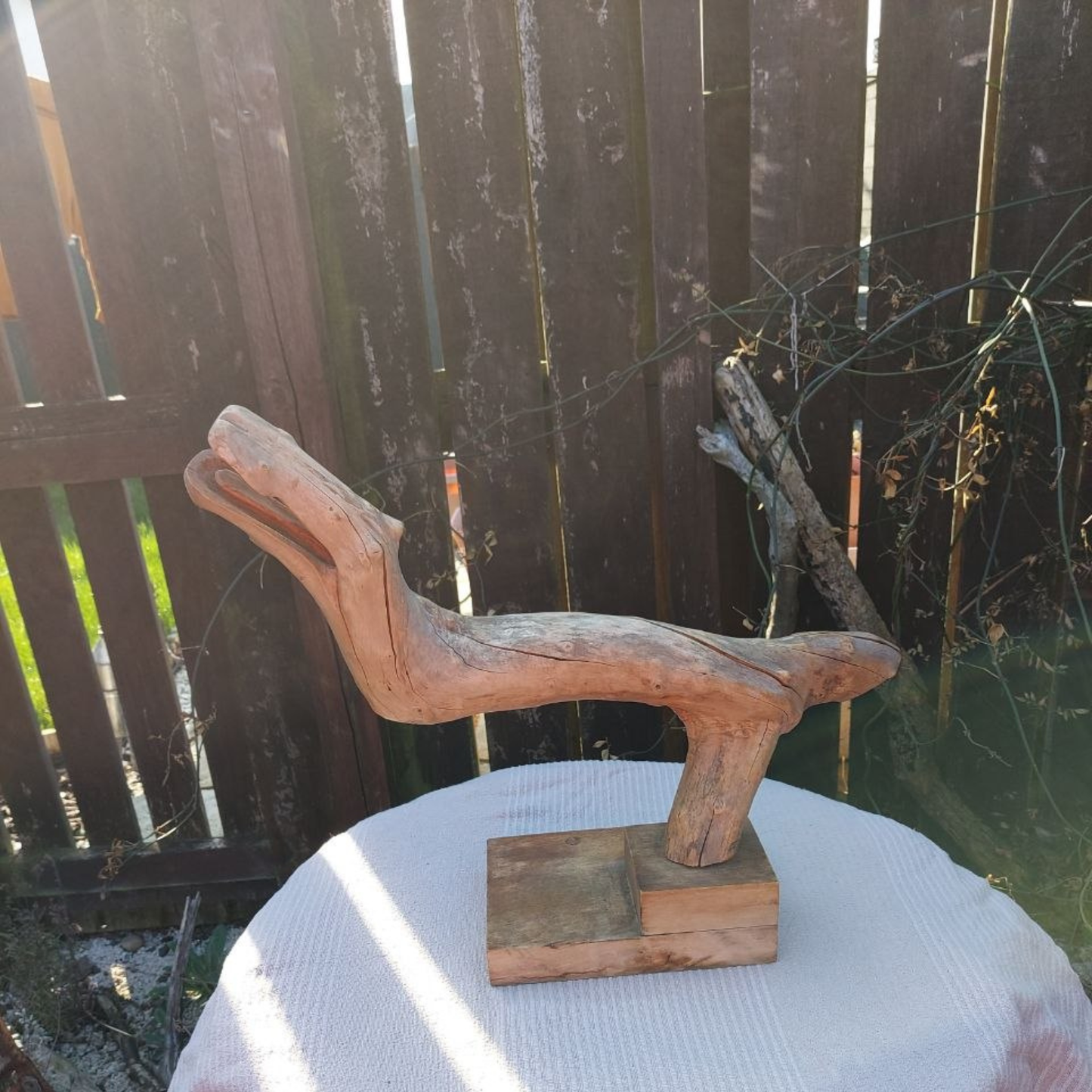 Wooden sculpture on a wooden base on a table outdoors. 