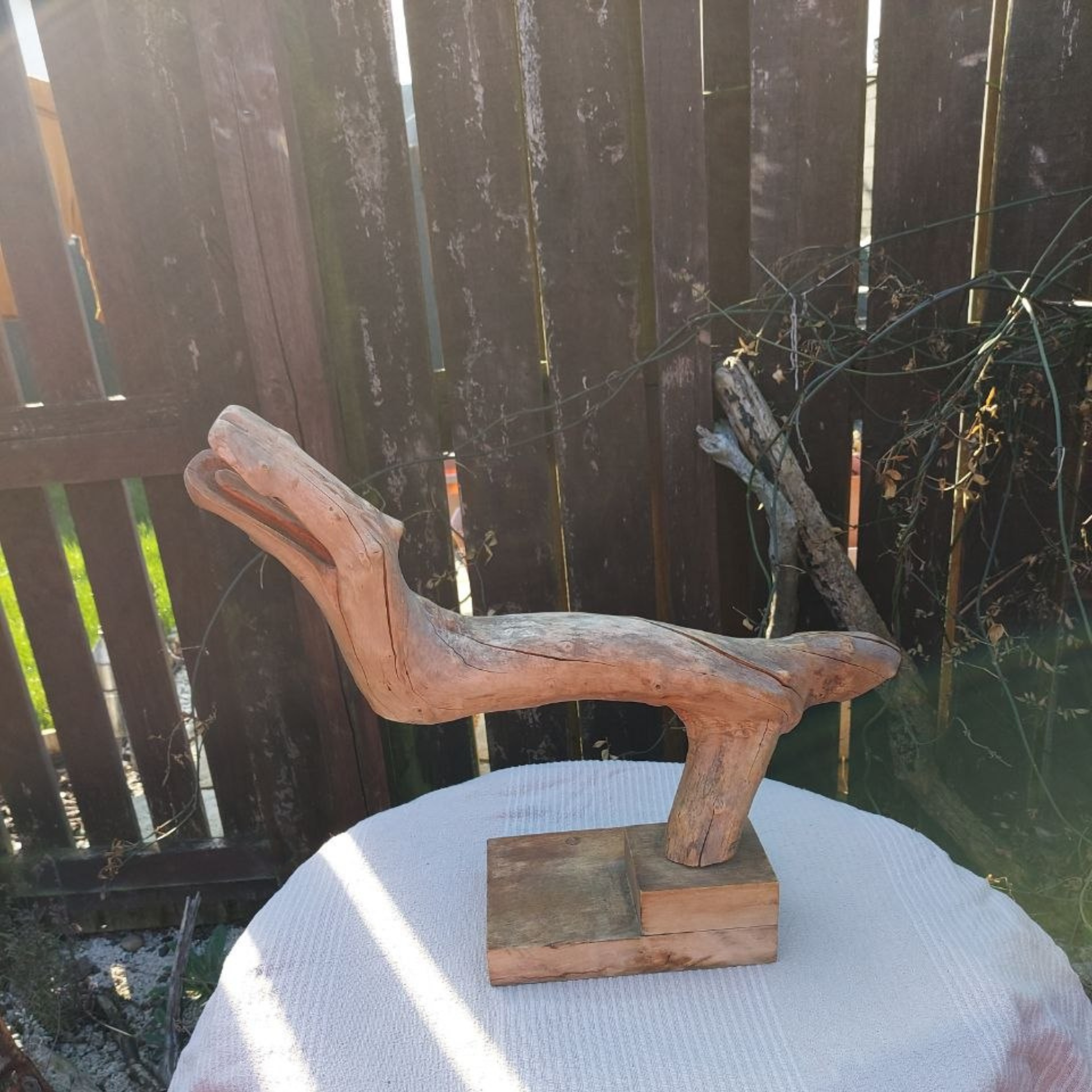 Wooden sculpture on a wooden base on a table outdoors. 