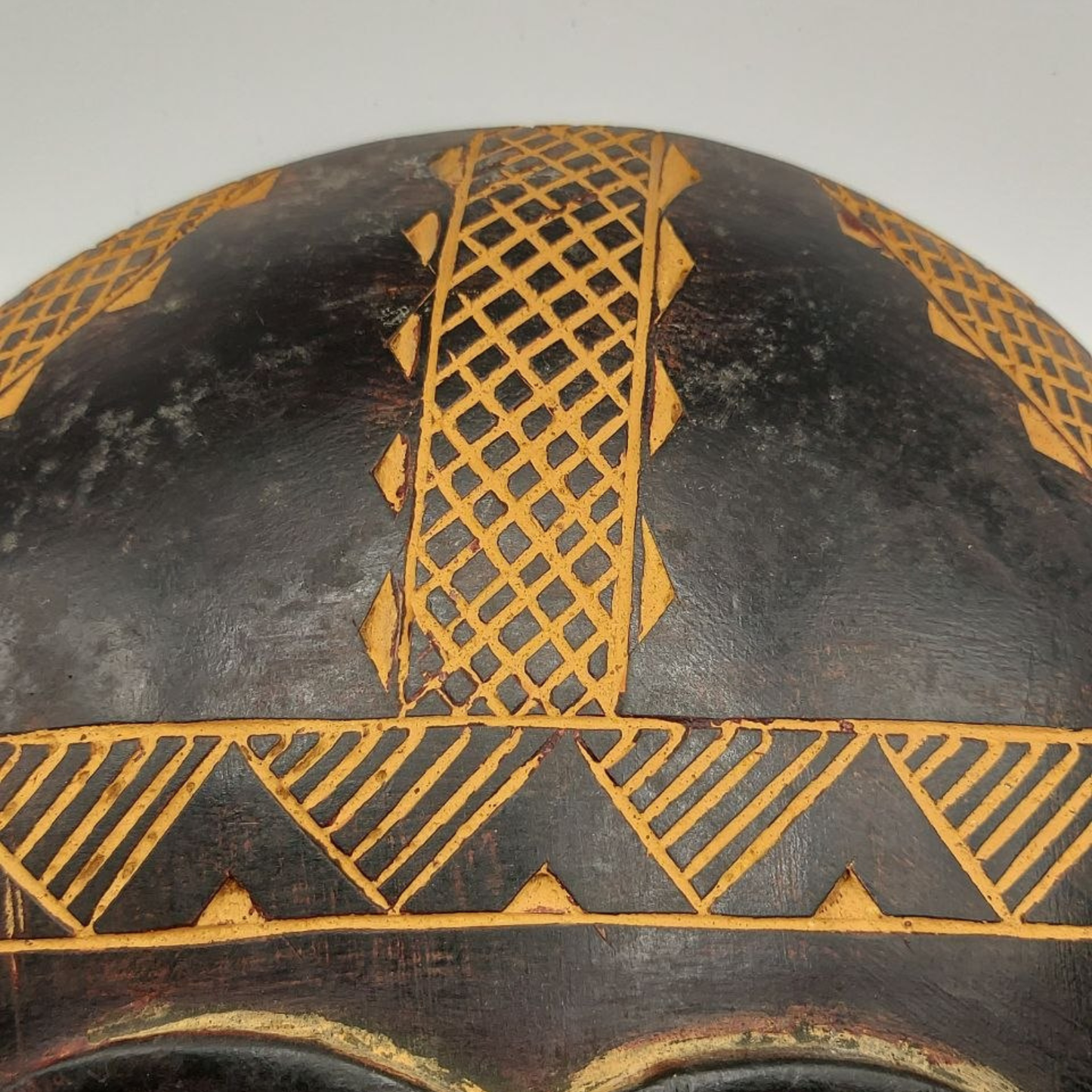Decorative wooden mask with geometric patterns on a plain background