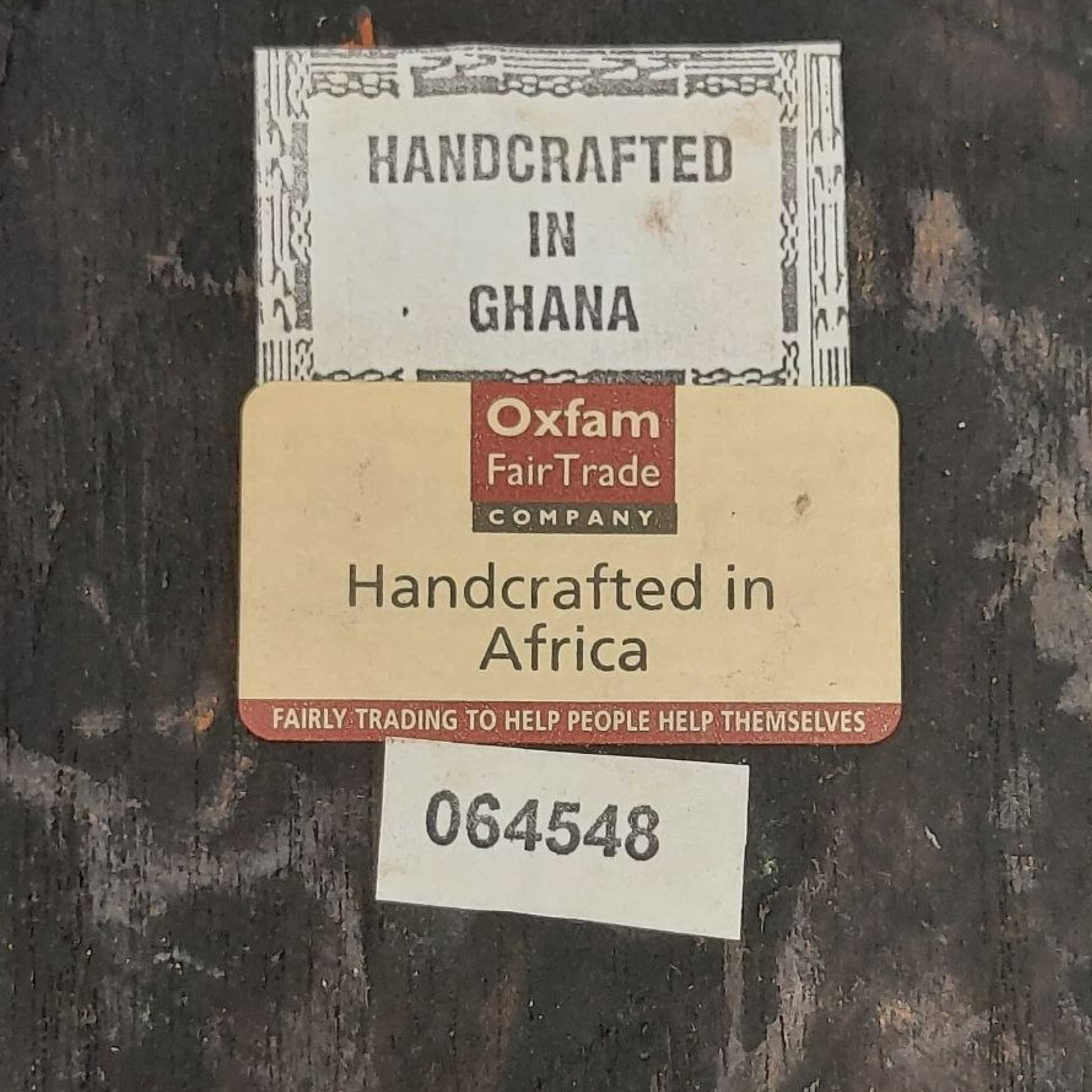 Three labels on a dark surface, with 'Handcrafted in Ghana' and 'Oxfam Fair Trade Company' visible.
