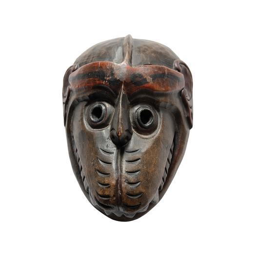 A carved wooden mask with a dark brown and black finish, featuring prominent circular eye openings and detailed facial carvings, isolated on a white background.