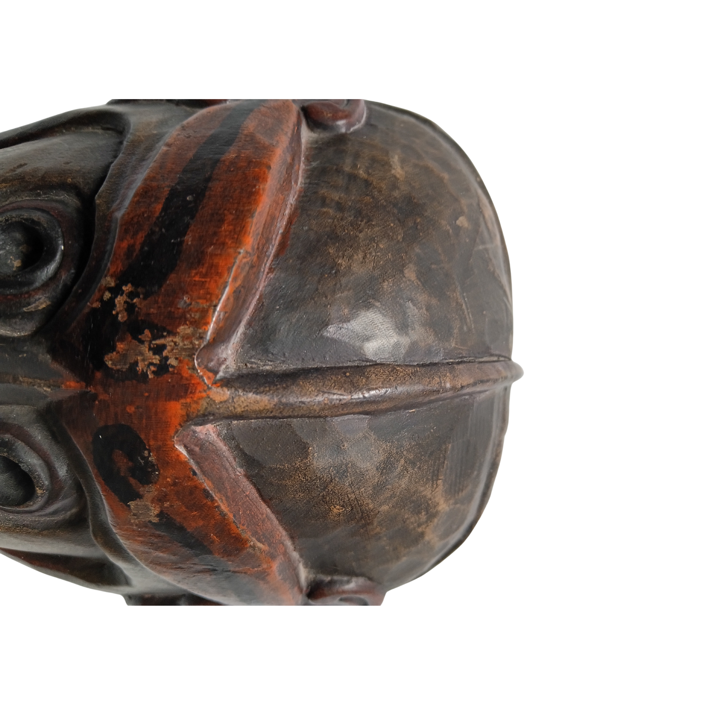 A close-up of a carved wooden mask with a dark brown and black finish and reddish-brown distressed accents, shown against a plain white background.
