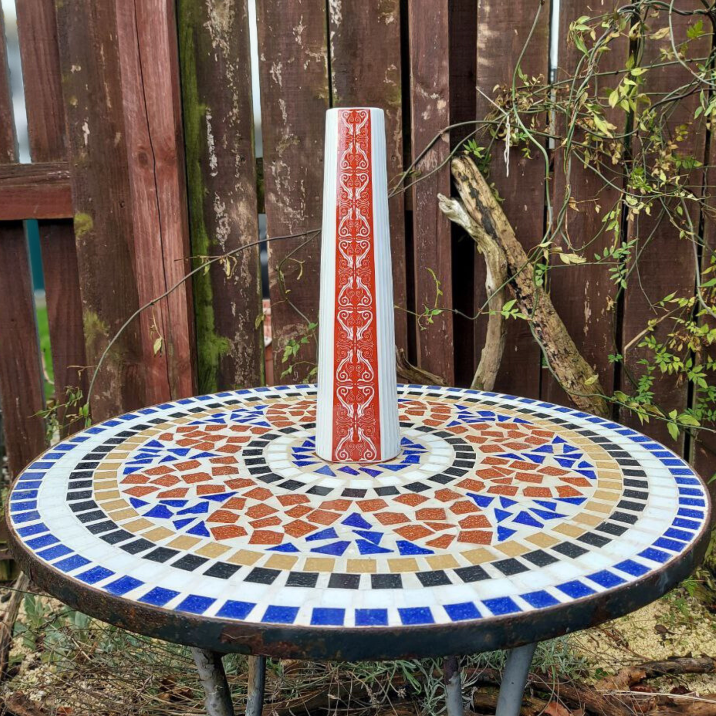 A decorative red and white Jaeger vase on a mosaic garden table. 