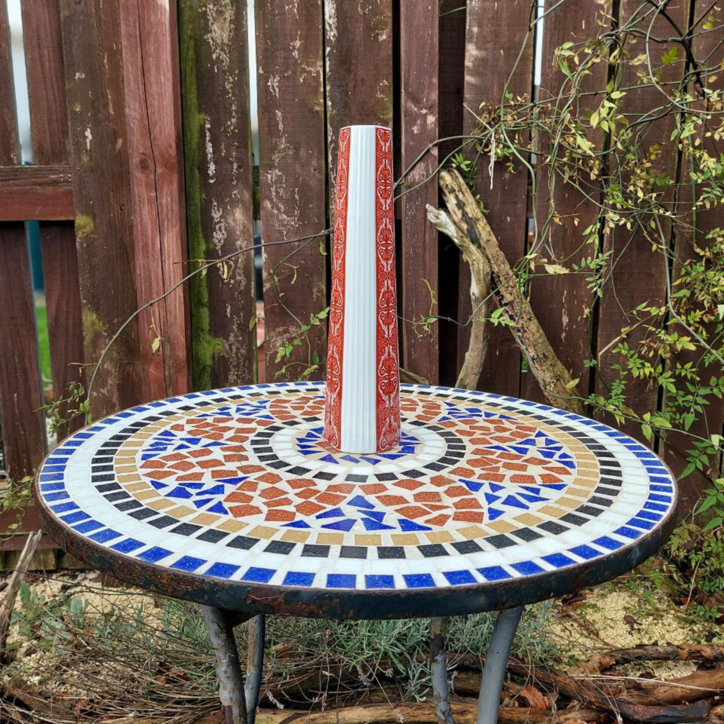 A red and white vintage vase on a mosaic garden table. 