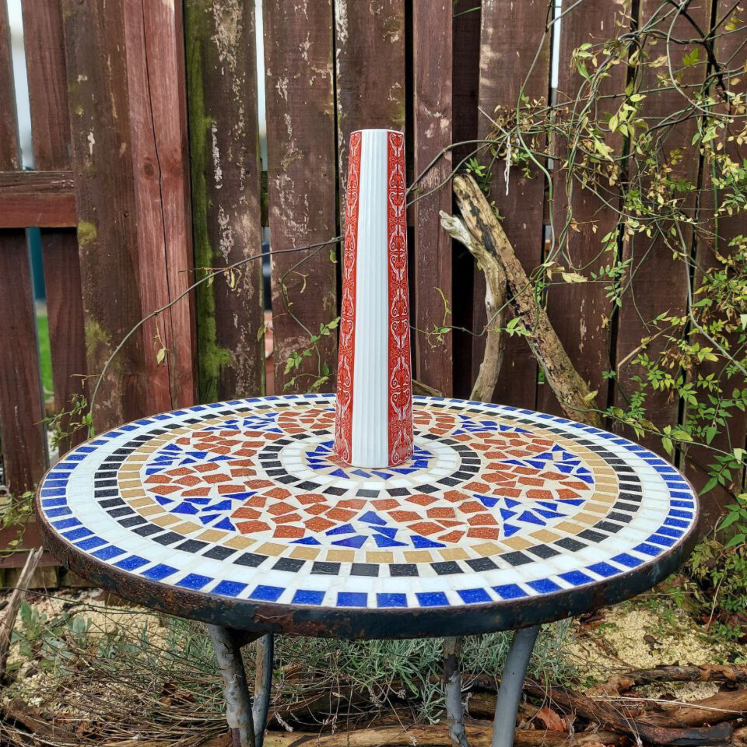 A red and white vintage vase on a mosaic garden table. 