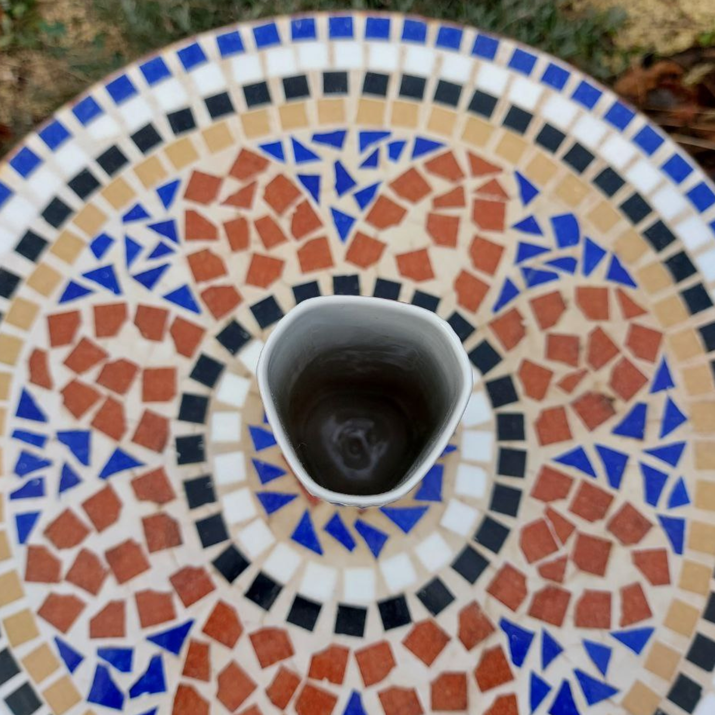 A top down view of a vintage vase on a mosaic table. 