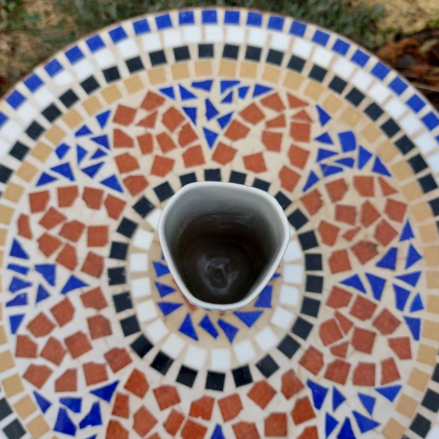 A top down view of a vintage vase on a mosaic table. 