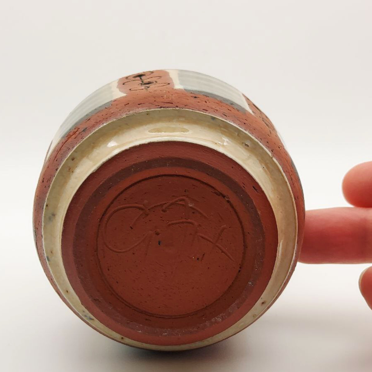 Ceramic vase with a red interior and beige exterior held by a hand on a white background