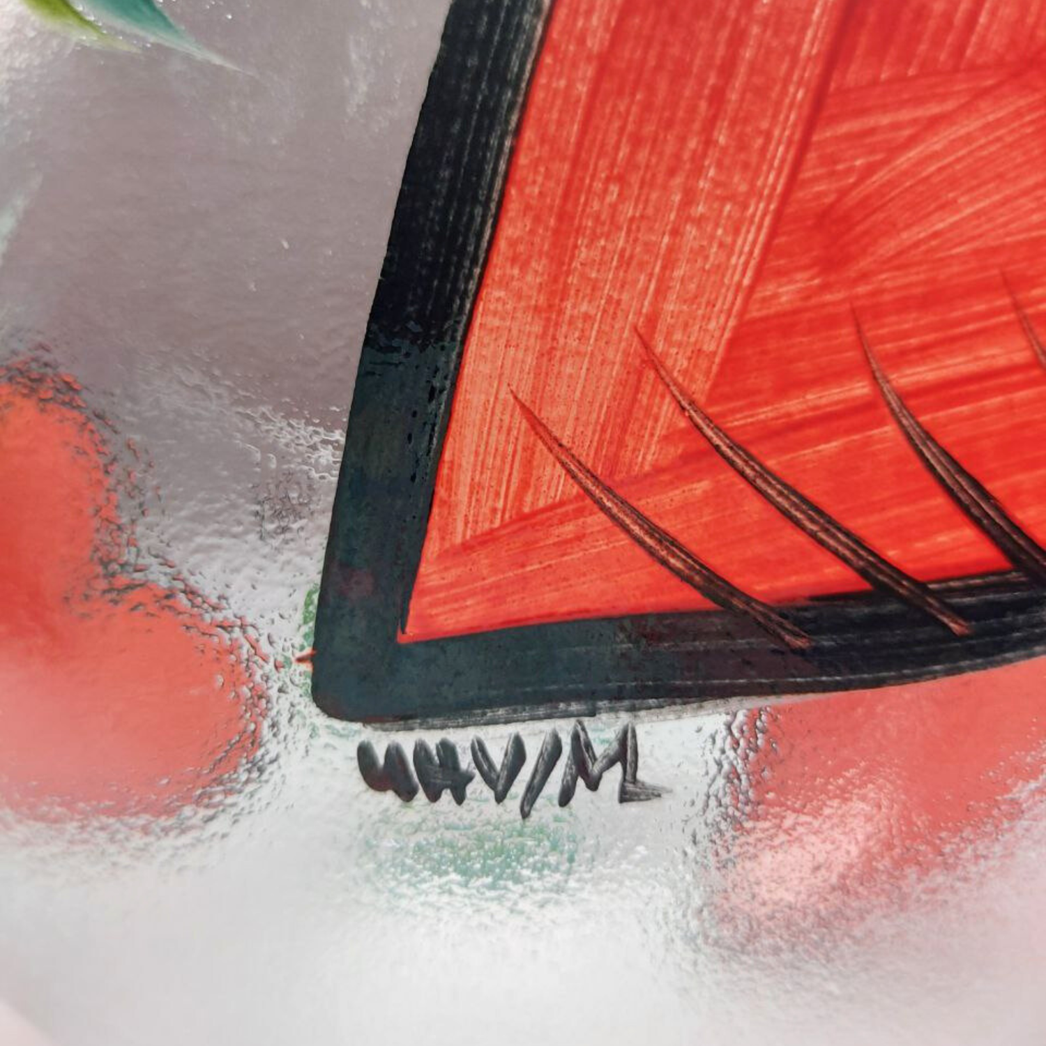 Close-up of a red and black glass bowl with a signature on a textured surface.