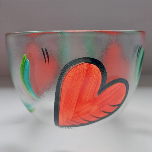 Decorative Kosta Boda glass bowl with hearts and colourful leaf patterns on a light background. 