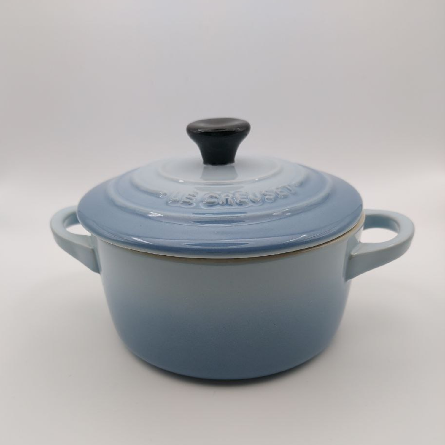 Blue enameled stoneware cooking pot with a black handle against a grey background