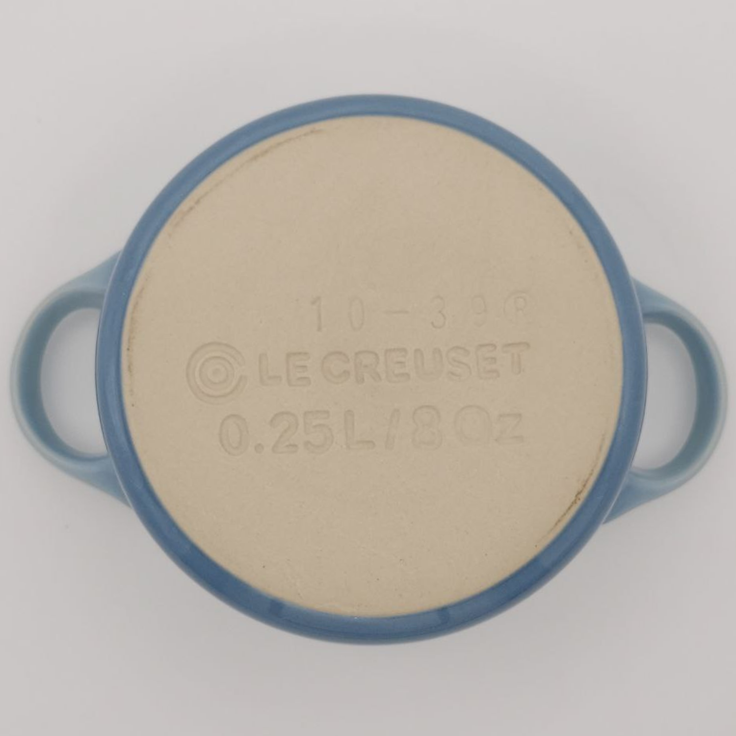 Round ceramic dish with blue rim and beige center, featuring Le Creuset branding.