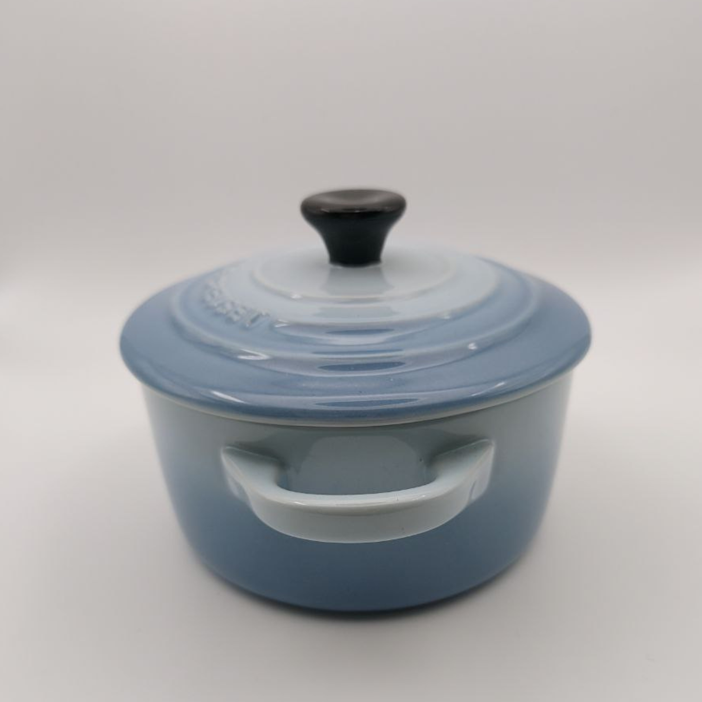 Blue enameled cast iron casserole dish with a black lid knob on a white background