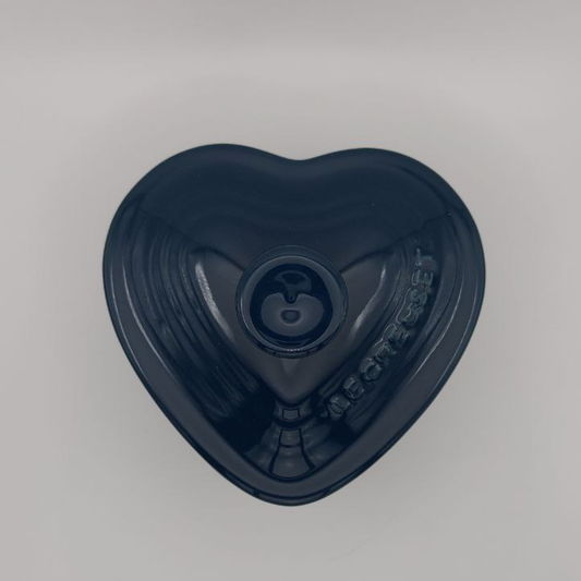 Dark blue heart-shaped Le Creuset cocotte with a brand logo on a grey background