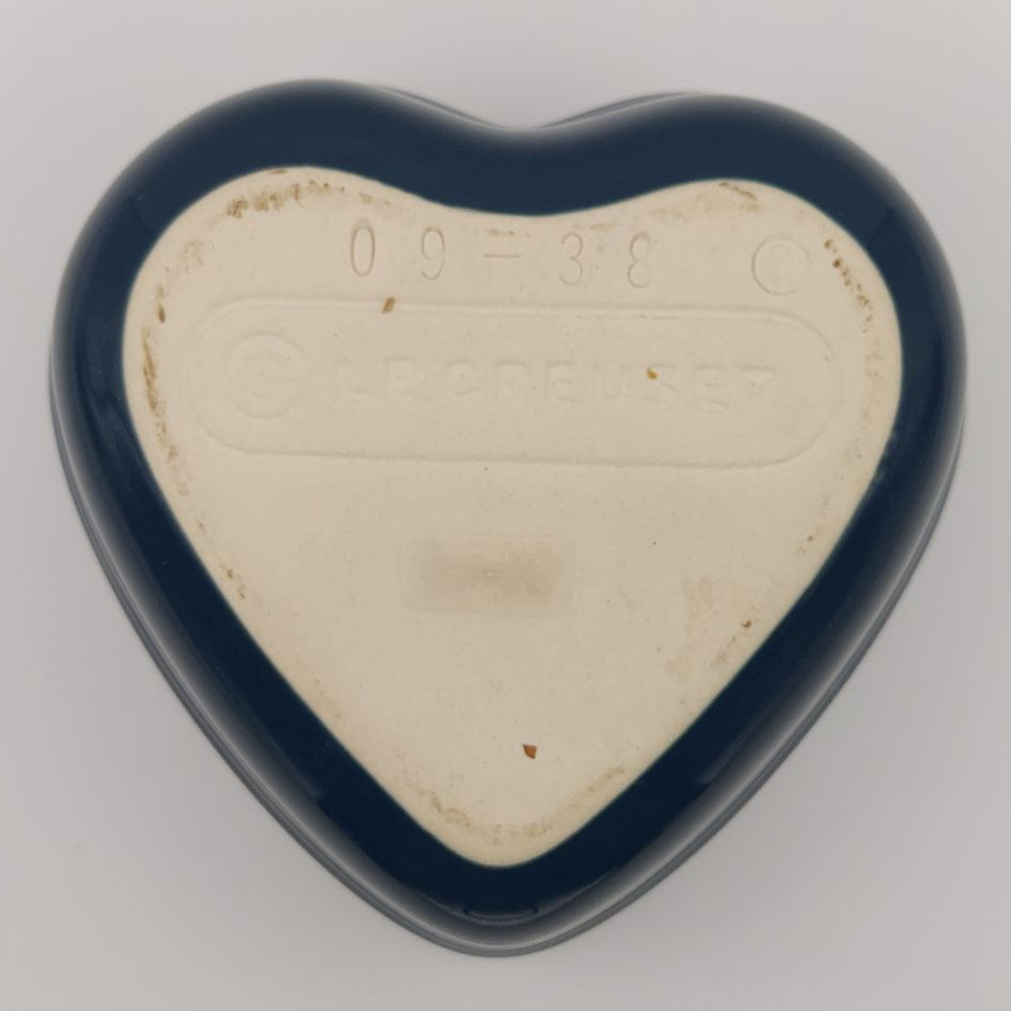 Heart-shaped stoneware cooking dish base on a light grey background. It says "09-38" and "Le Creuset"